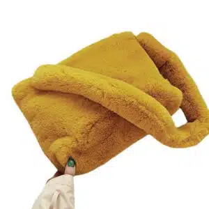Un sac en fausse fourrure de couleur jaune posé à plat. Par-dessus repose sa hanse en fourrure également. Une main de femme tient le sac par le bas.