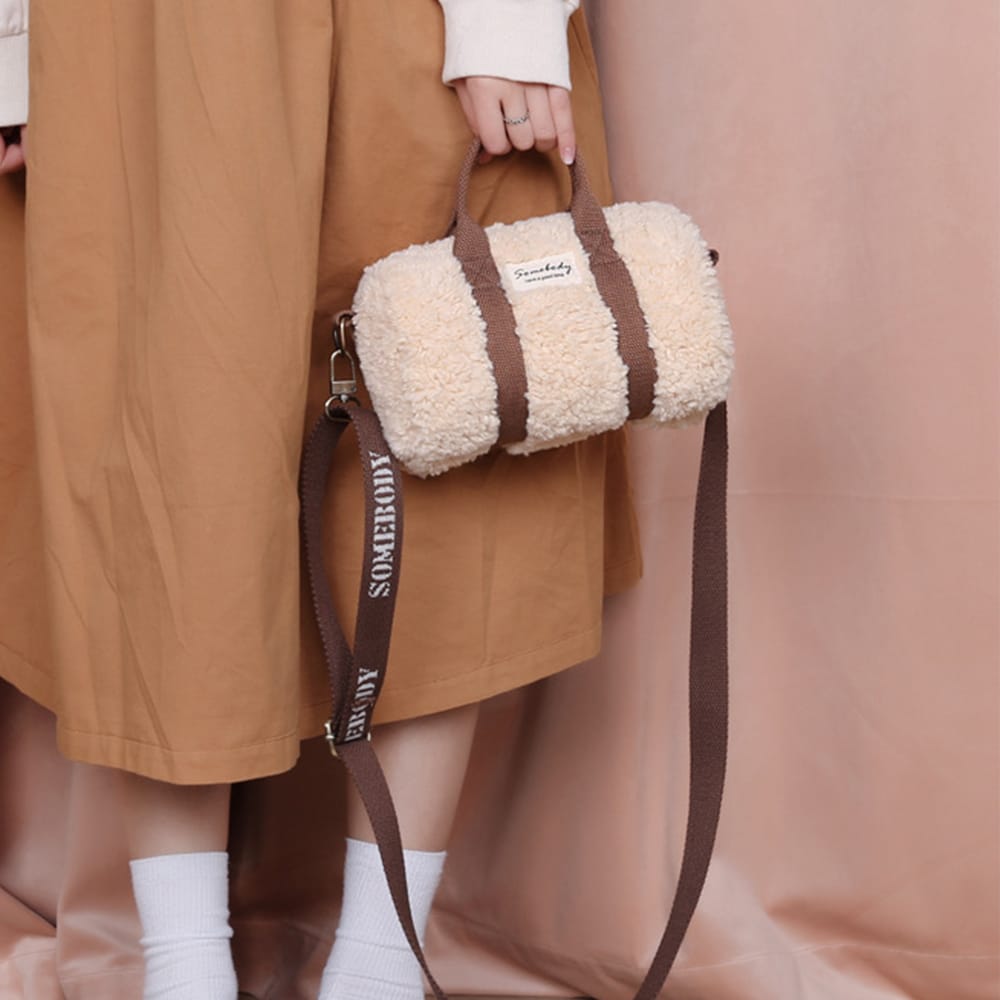 Petit sac à main de luxe imitation laine d'agneau rose porté par une femme en robe orange