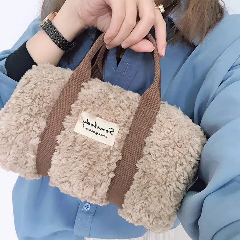 Petit sac à main de luxe imitation laine d'agneau kaki mis en avant par une femme luxueuse avec un chemisier bleu