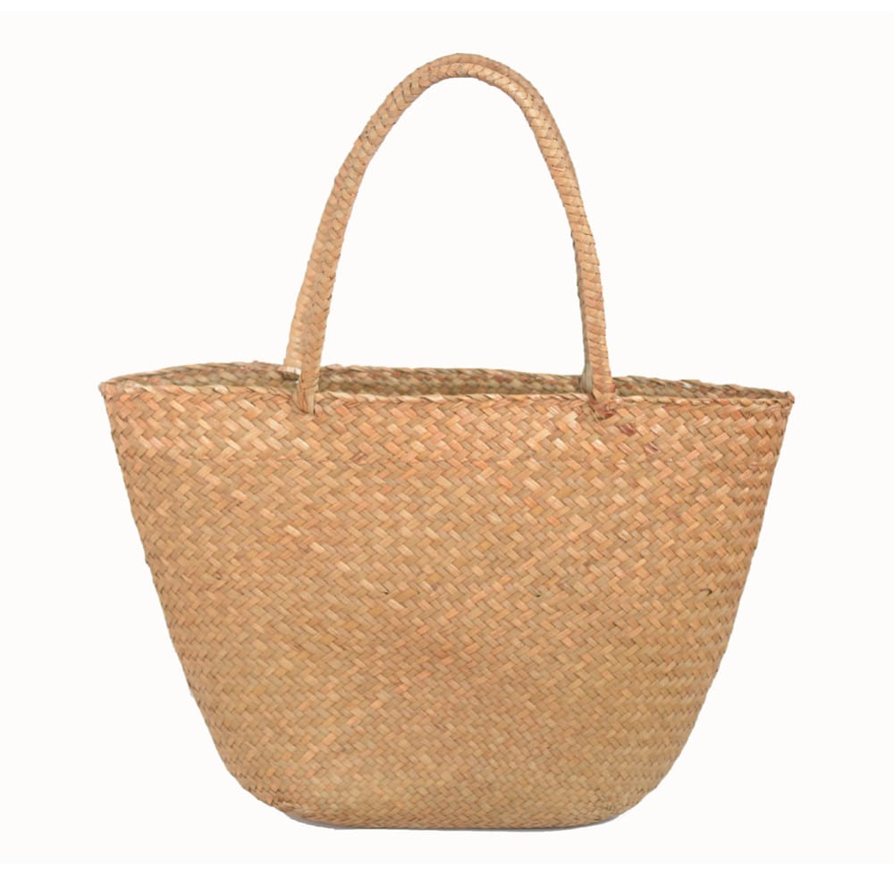 Un sac à main de plage en paille de forme arrondi vintage, il est de couleur marron clair et a deux hanses dans le même coloris sur le dessus.