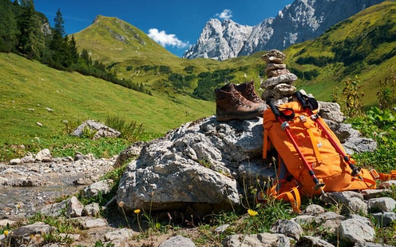 Photo dans la nature près des montagnes, une paire de chaussures de marche et un sac de randonnée avec des bâtons de marche, posés sur un rocher.